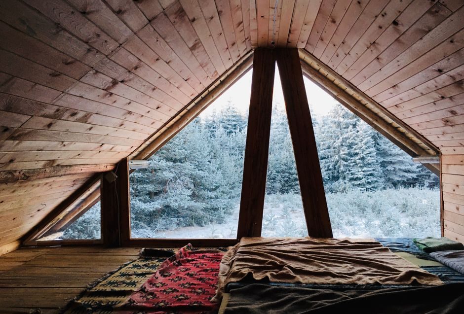 Warm attic room in wooden cabin with blankets overlooking a snowy forest.
